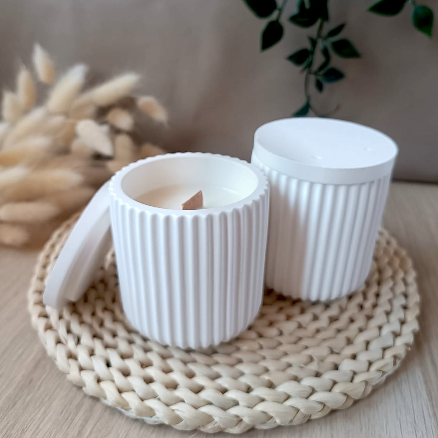 Dos vela de soja en recipiente blanco de resina mineral con diseño de rayas verticales y tapa lisa sobre base de fibras naturales y fondo neutro