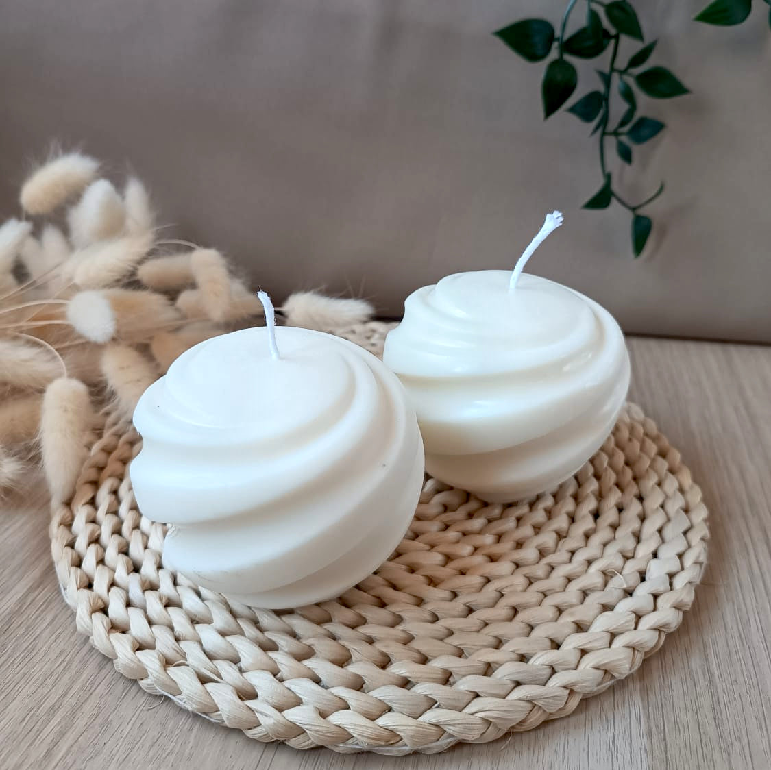 Dos velas decorativas de soja redondas grandes con diseño en espiral sobre base de fibras naturales y fondo neutro
