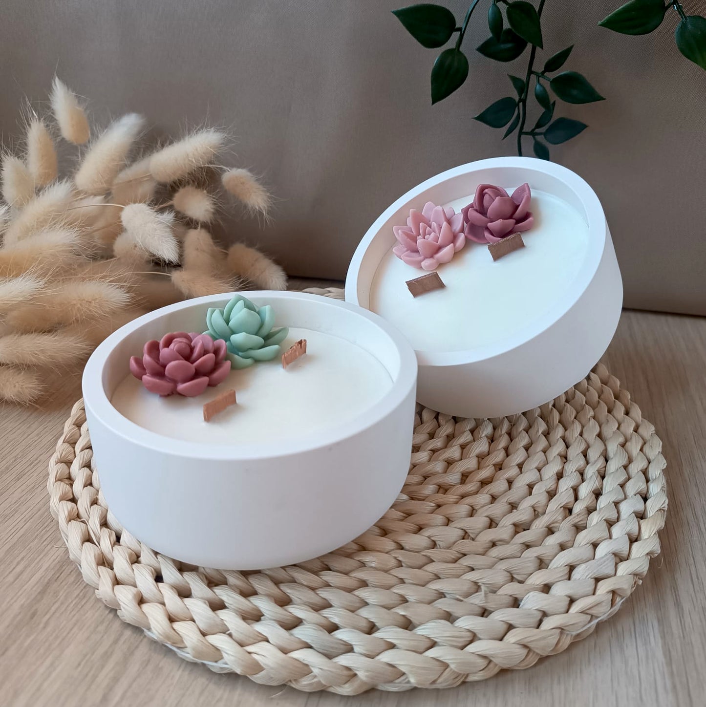 Dos velas decorativas de soja en recipiente de resina mineral con doble mecha de madera y suculentas sobre base natural y fondo neutro