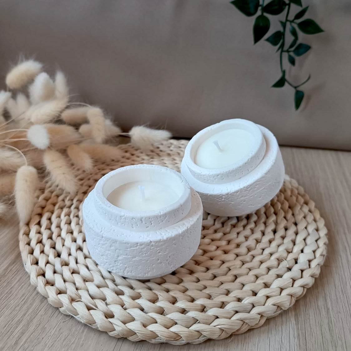 Dos velas de soja en recipientes blancos con textura rugosa efecto lava y mecha de algodón sobre soporte de fibras naturales y fondo neutro